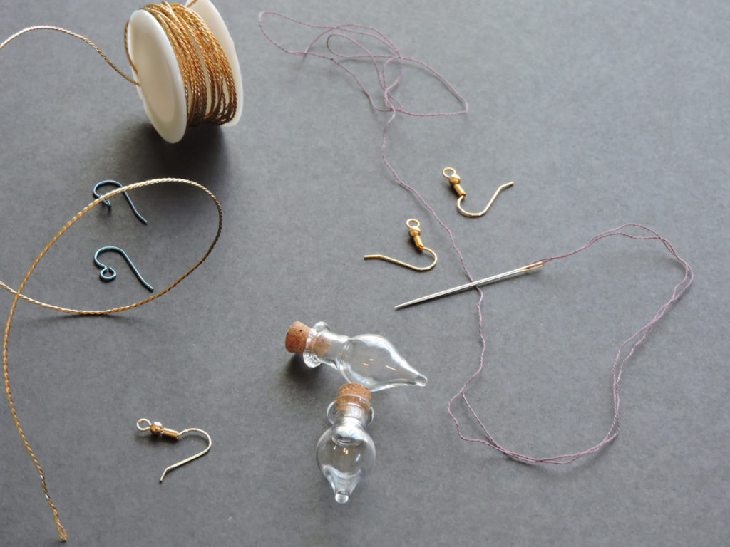 display of earring hooks, small glass vials, needle and thread, jewelry wire