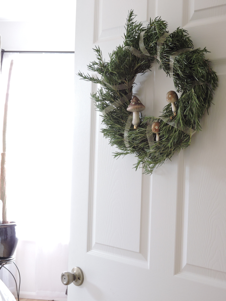 rosemary wreath with pink ribbon and mushroom ornaments hanging from door