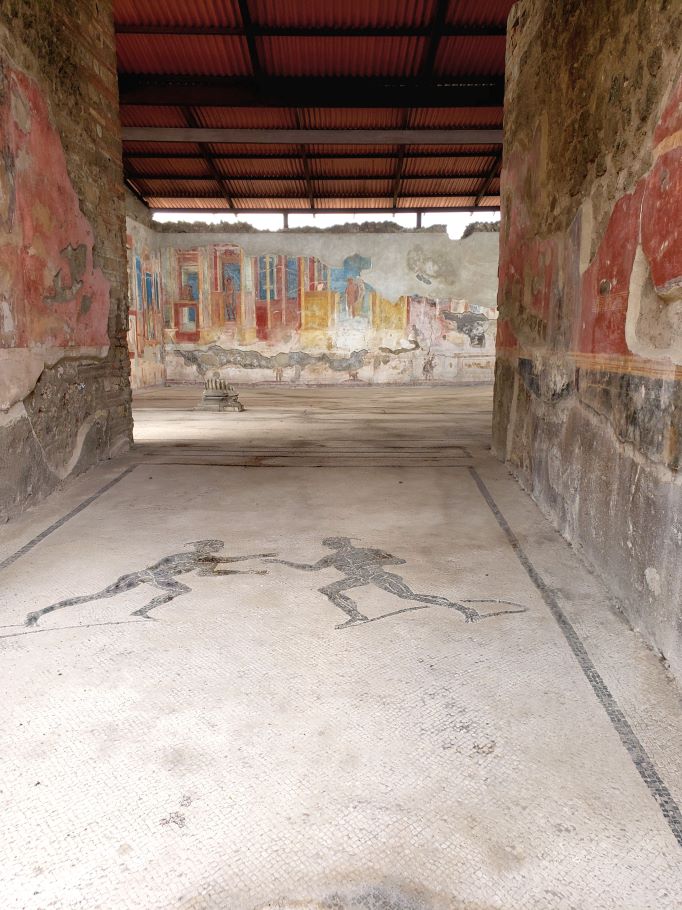 mosaic floor with two figures fighting and colorful painted walls inside the gymnasium of the luvenes