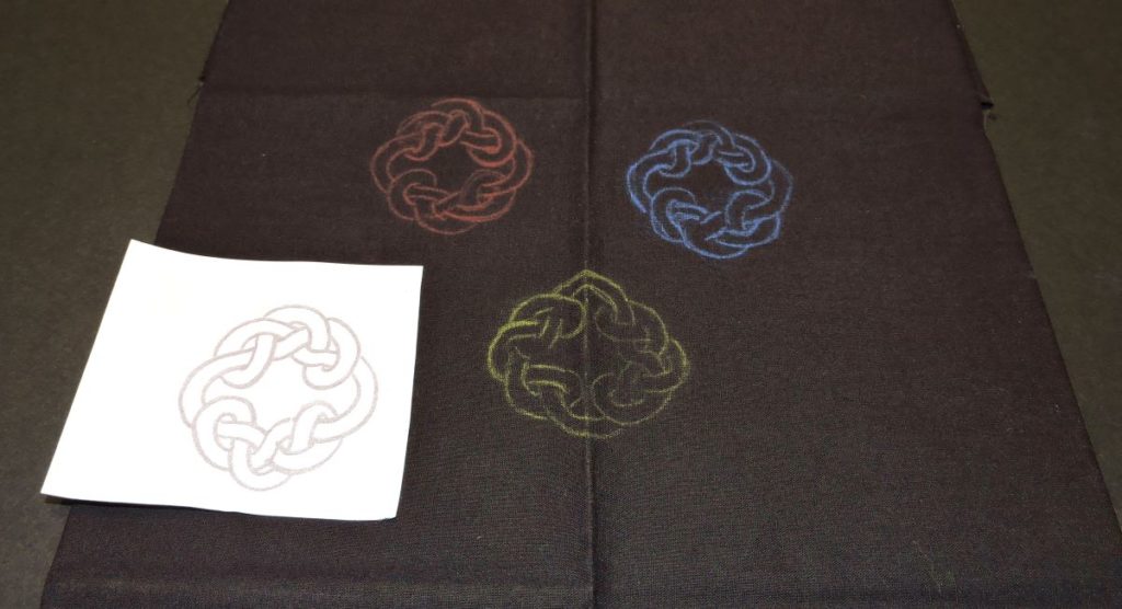 red blue and yellow designs transferred onto dark black fabric using transfer paper